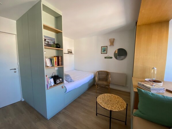 Ein gemütlicher Raum mit einem Bett, einem Bücherregal, einem Sessel und einem kleinen Tisch.