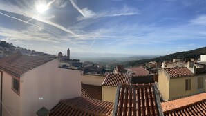 A view of terracotta-tiled rooftops, a church with a bell tower, and a distant landscape under a clear sky. - Welcomely - Casa Vania (Bolotana)