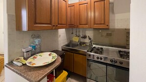 A kitchen with wooden cabinets, a stainless steel sink, a stove, and a microwave. - Welcomely - Casa Vania (Bolotana)