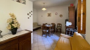 A dining area with a table set for four, a sofa, and a cabinet with a television. - Welcomely - Casa Vania (Bolotana)