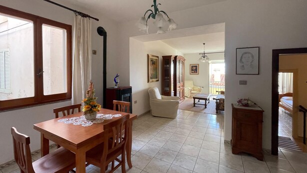 A spacious living area with a dining table, chairs, a sofa, and a chair. There is a staircase leading to another level. - Welcomely - Casa Vania (Bolotana)