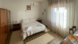 A bedroom with a bed, two bedside tables, a wooden wardrobe, a chandelier, and a window with sheer curtains. - Welcomely - Casa Vania (Bolotana)