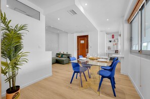 Un salon moderne avec une table à manger en verre, des chaises bleues, un canapé vert et une plante en pot.