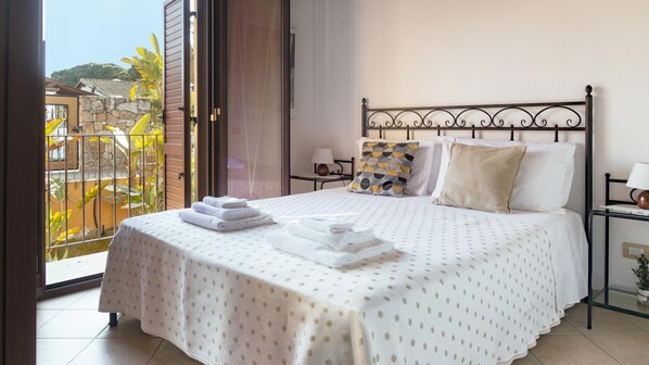 A hotel room with a bed, a nightstand, a lamp, and a view of a balcony with plants. - Welcomely - S Ogiastru-l Olivastro (Tortoli)