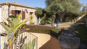 A stone building with a tiled roof, a garden with various plants, and a large stone planter. - Welcomely - S Ogiastru-l Olivastro (Tortoli)