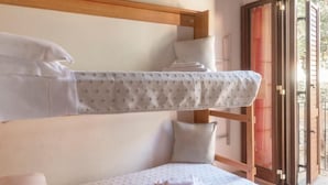 Una cama litera con estructura de madera y colchón blanco estampado con lunares. Hay almohadas en la cama y una ventana con vistas a la vegetación.