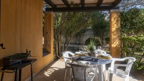 An outdoor patio with a table set for dining, surrounded by white plastic chairs, and a small black table with a plant. - Welcomely - S Ogiastru-l Olivastro (Tortoli)