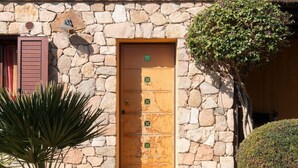 Un edificio de piedra con puerta de madera, una ventana con contraventanas y una planta en maceta.