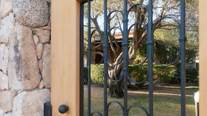 Una reja de hierro forjado con un muro de piedra y un árbol al fondo.