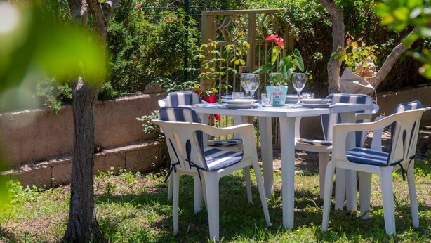 Uma área de refeições ao ar livre com uma mesa redonda e quatro cadeiras, rodeada por vegetação e um cercado de madeira.