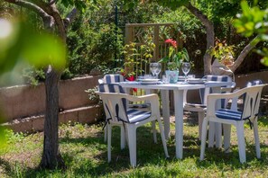 Un área de comedor al aire libre con una mesa redonda y cuatro sillas, rodeada de follaje y una valla de madera.