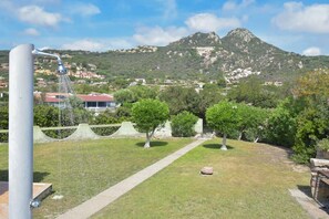 A grassy area with a pathway leading to a mountain. There is a water fountain and a tall pole in the foreground.