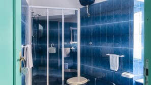 Une salle de bain avec des carreaux bleus, une douche en verre, des toilettes et un lavabo.