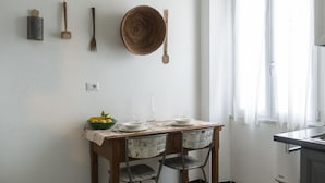 Un coin repas avec une table en bois, des chaises, un saladier rempli de fruits et une nappe recouverte de journaux.