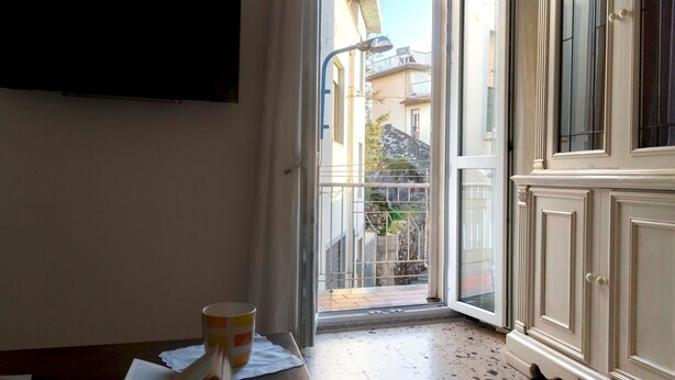 Une pièce dotée d’une porte-fenêtre coulissante donnant sur un balcon, d’une armoire blanche et d’une table sur laquelle se trouvent une tasse et un livre.