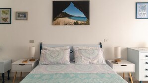 Une chambre à coucher comprenant un lit, deux tables de chevet, une commode et un tableau représentant une plage, accroché au mur.