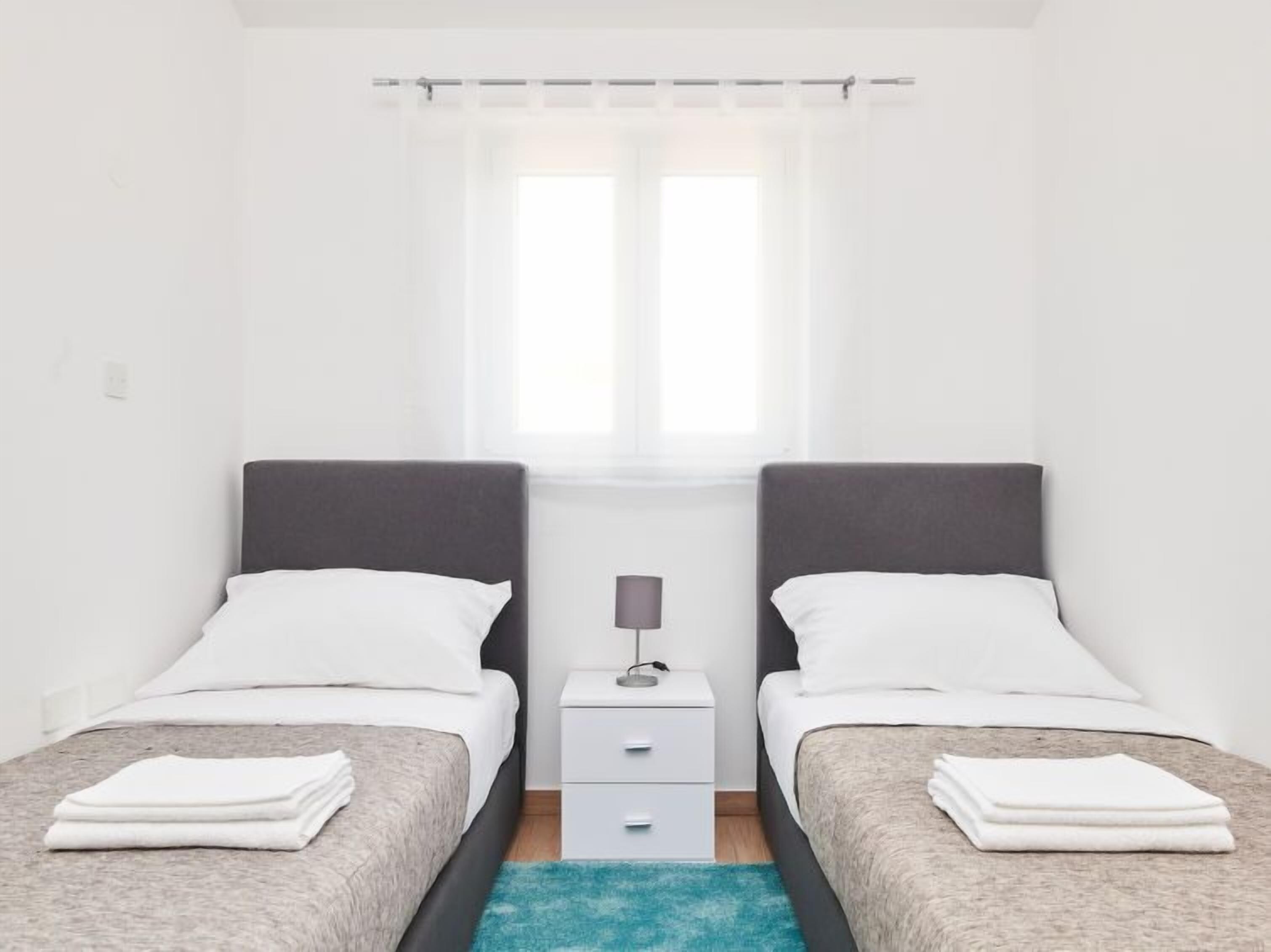Une chambre double avec deux lits, une table de chevet, une lampe et une fenêtre avec des rideaux légers.