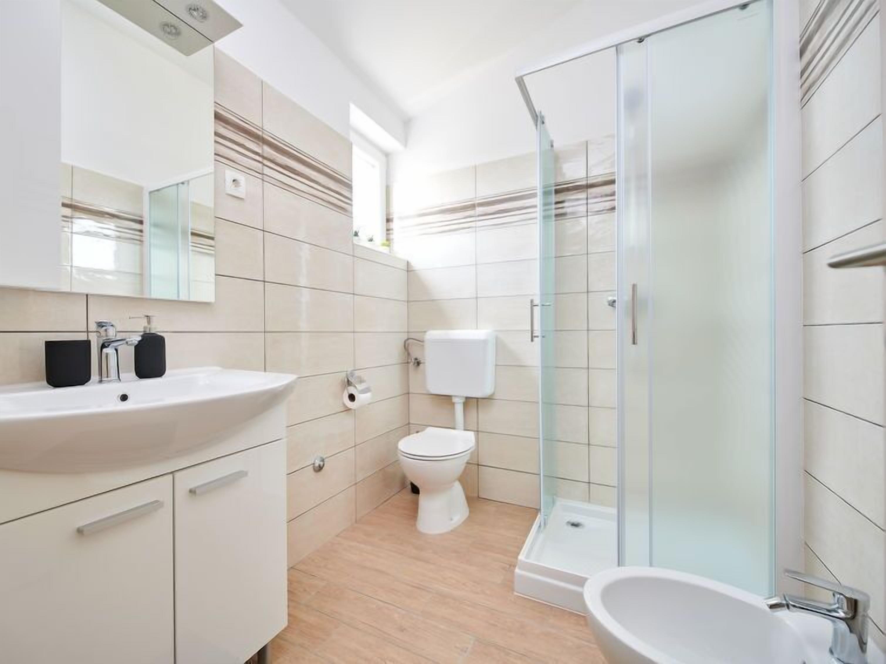 A modern bathroom with a white sink, toilet, and shower.