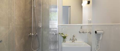A modern bathroom with a glass-enclosed shower, a sink with a mirror, and a hairdryer mounted on the wall.