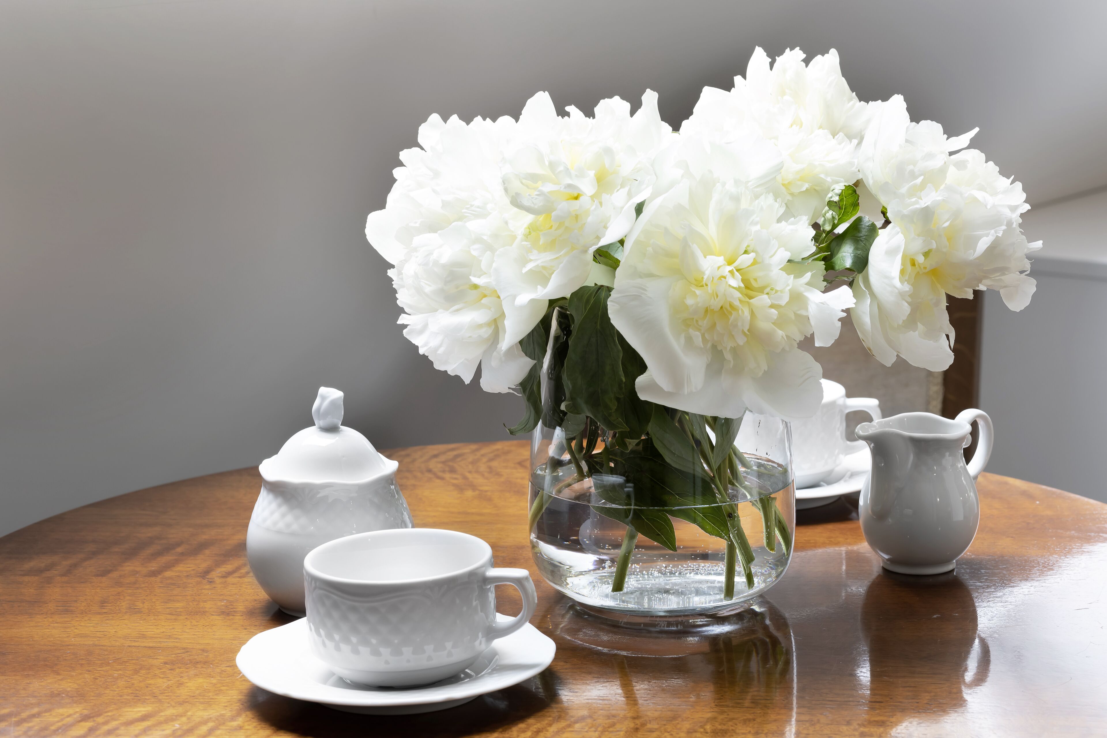 A table with a white teapot, a cup, a pitcher, and a vase with white flowers.