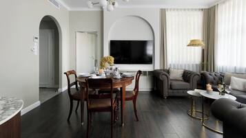Una sala de estar moderna con piso de madera oscura, una mesa de comedor redonda con sillas, un sofá gris y un televisor montado en la pared.