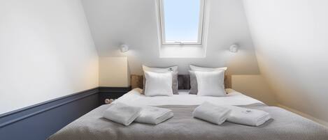 A bedroom with a skylight, a bed with white linens, and two bedside lamps.