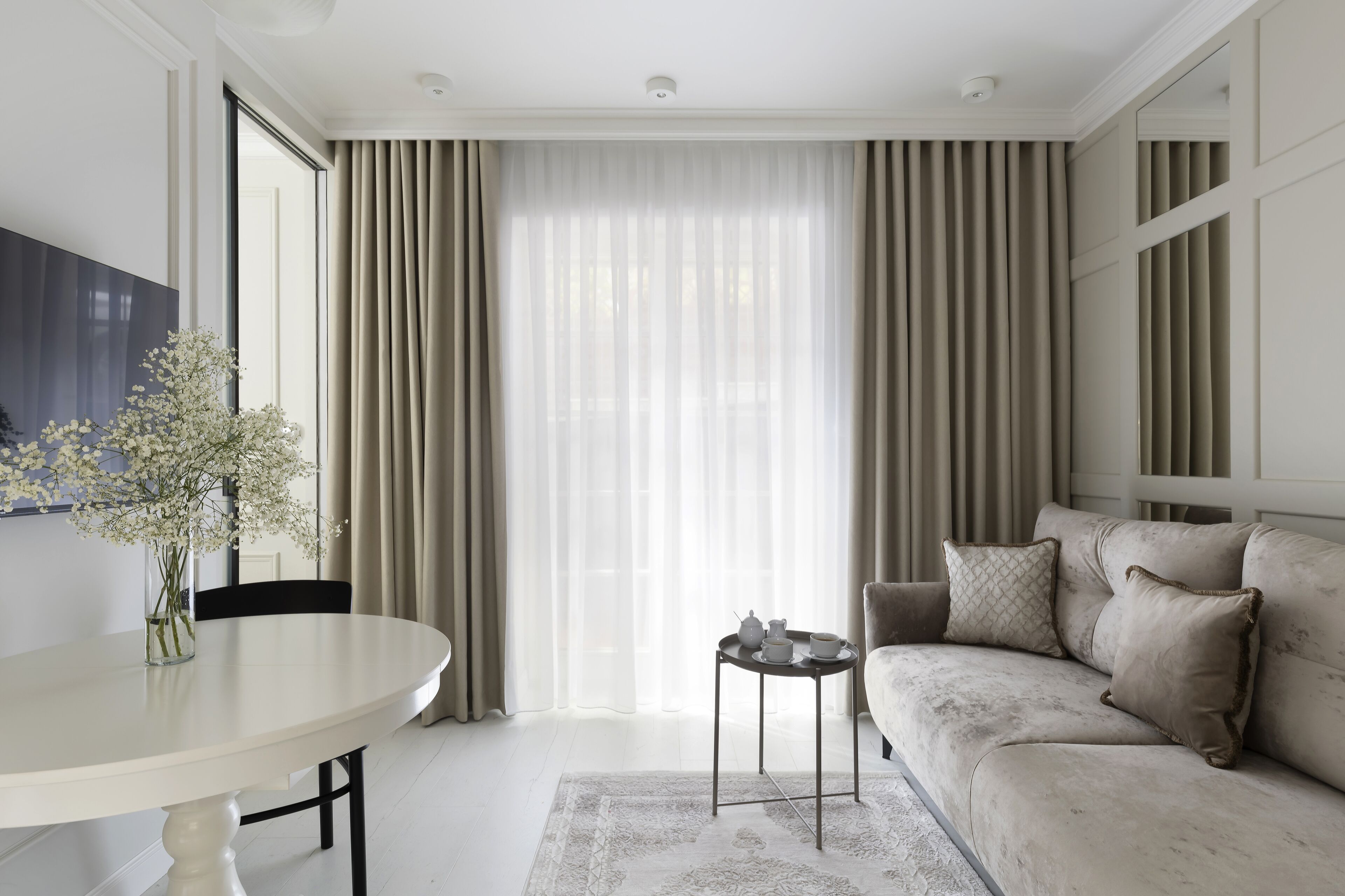 A modern living room with a white round table, beige sofa, and a small side table with a teapot.