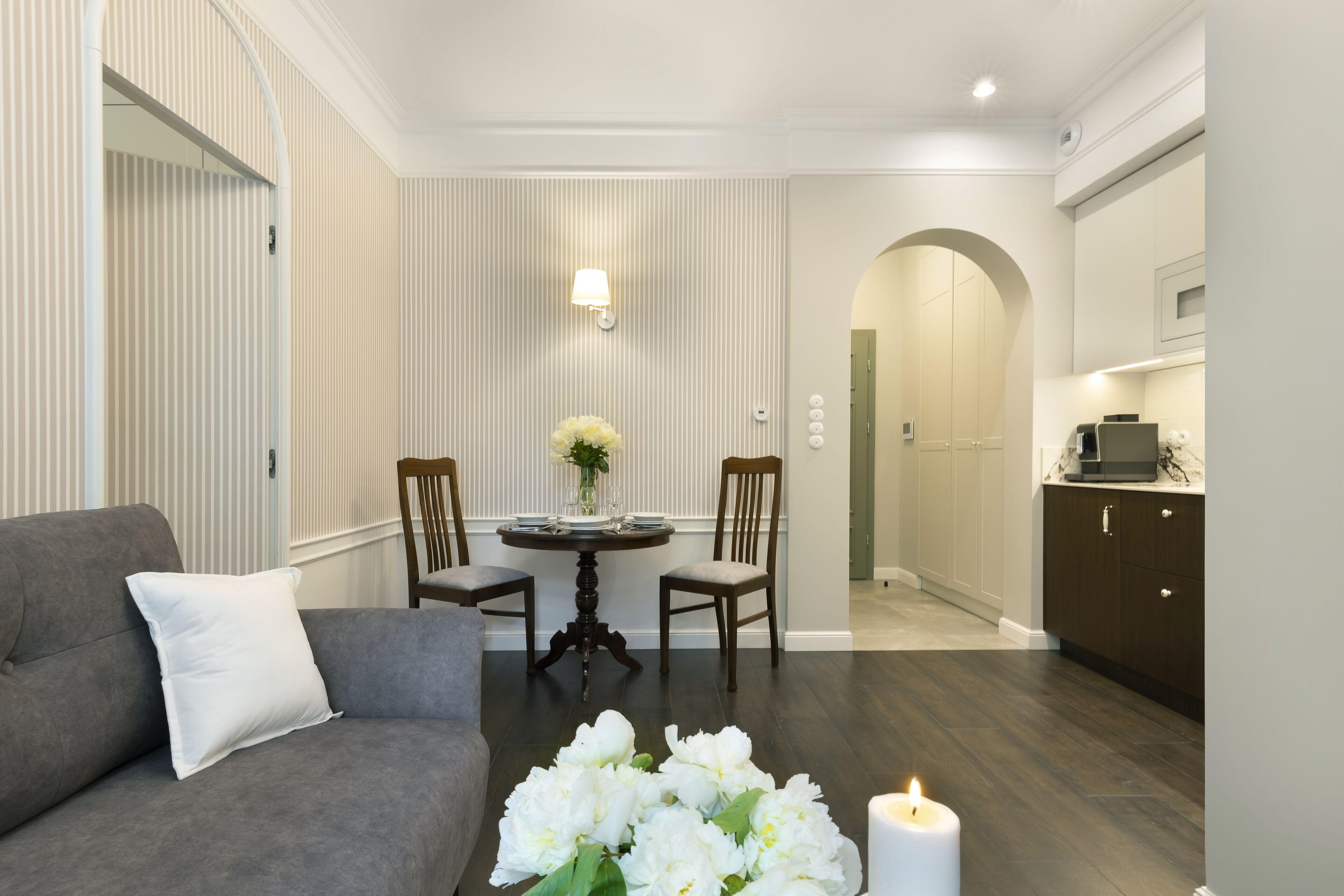 Ένα σαλόνι με έναν γκρι καναπέ, ένα στρογγυλό τραπέζι με καρέκλες και ένα βάζο με λουλούδια.