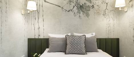 A neatly made bed with a green headboard, two wall-mounted lamps, and a wall with a floral pattern.