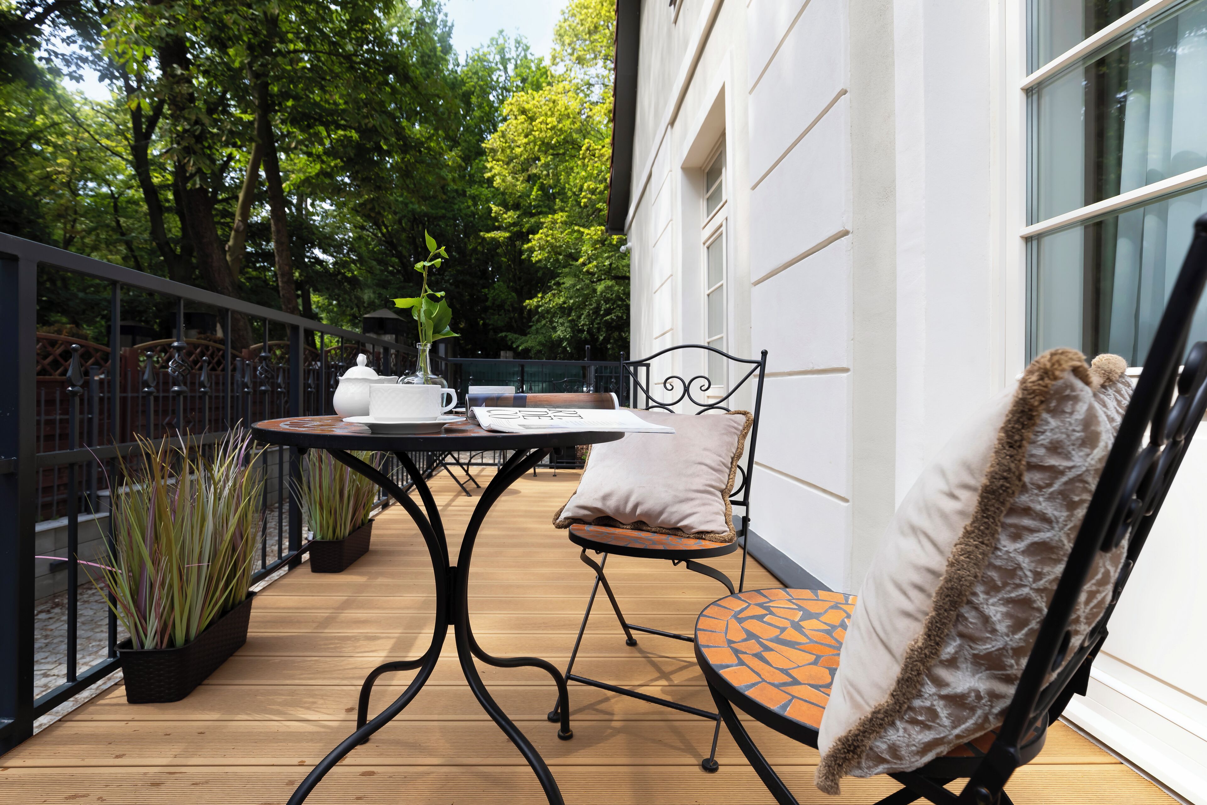 An outdoor patio with a table and chairs, surrounded by potted plants and a white building in the background.