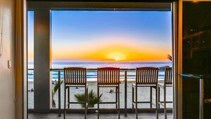 Un balcon avec trois chaises en bois donnant sur un coucher de soleil sur l’océan.