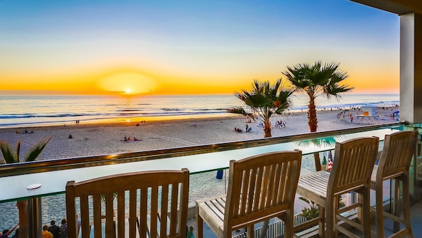 Un balcon avec des chaises en bois donnant sur une plage au coucher du soleil.
