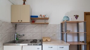 Una cucina compatta con lavandino, fornello e pensili. Sopra il bancone, degli scaffali contengono diversi oggetti da cucina.