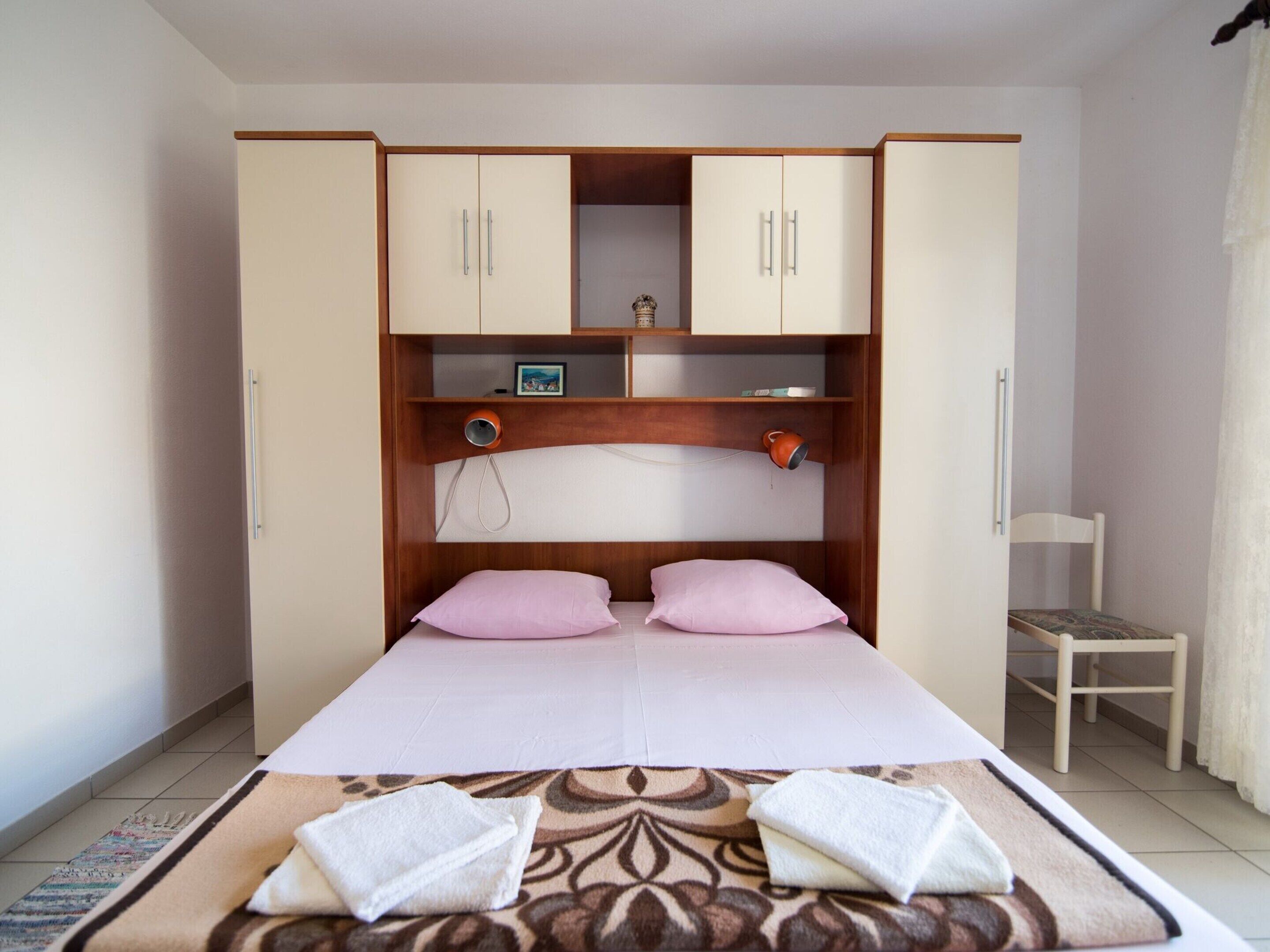 Een slaapkamer met een bed, twee kussens, een nachtkastje met een lamp en een garderobe met twee deuren.