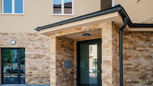 L'ingresso di un edificio con facciata in pietra, una porta in vetro e un piccolo sporgere sopra la porta.
