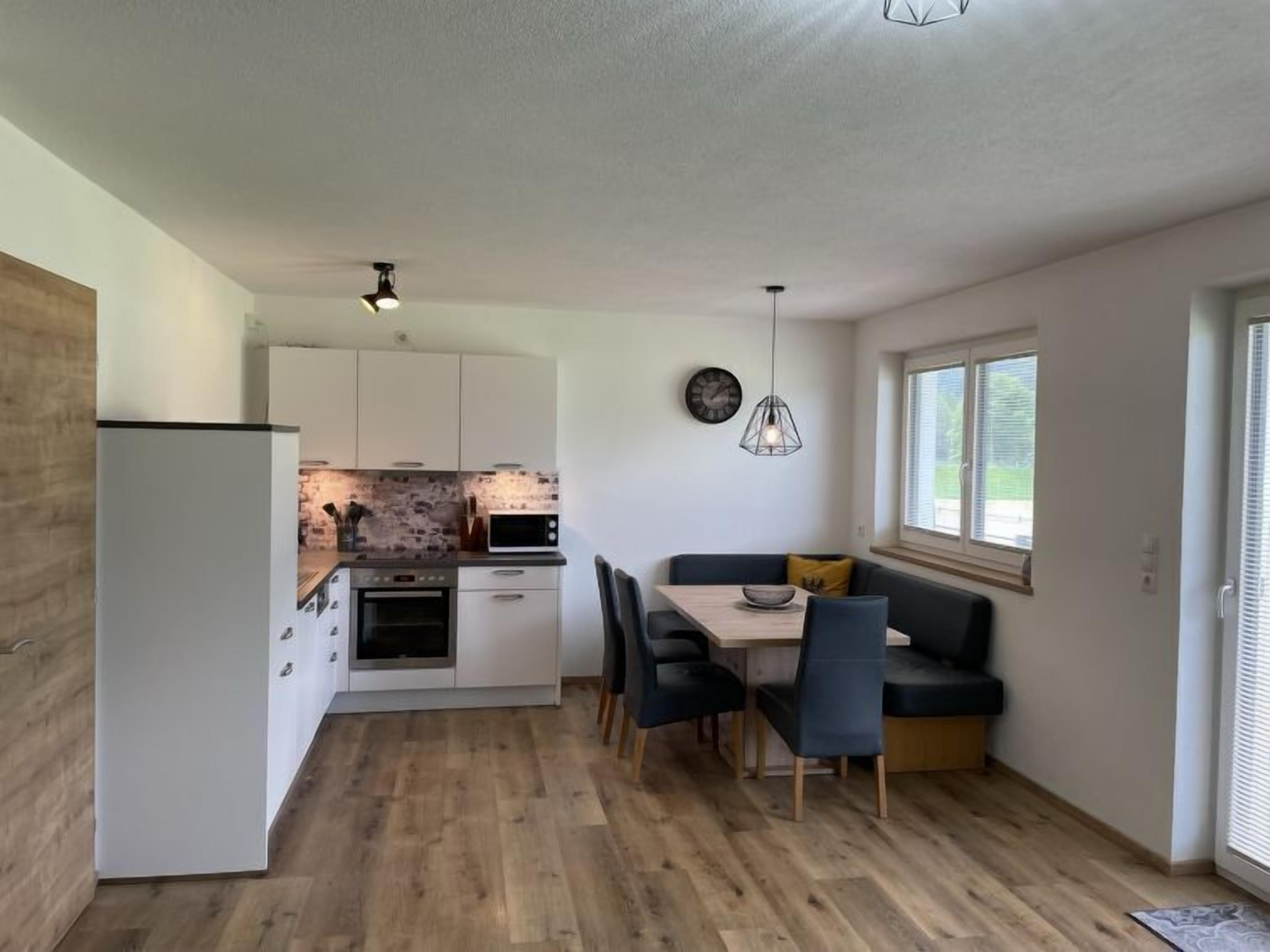 Een moderne keuken met witte kasten, een inbouwoven en een magnetron. Er is een zithoek met een tafel en stoelen, en een bank tegen de muur.