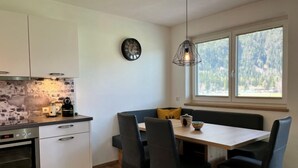 A compact kitchen with white cabinets, a built-in oven, a brick backsplash, and a dining area with a table and chairs. - Apartment Aiko by Interhome (Längenfeld)