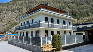 A two-story building with a balcony, surrounded by a stone wall and a wooden fence, set against a mountainous backdrop. - Apartment Aiko by Interhome (Längenfeld)