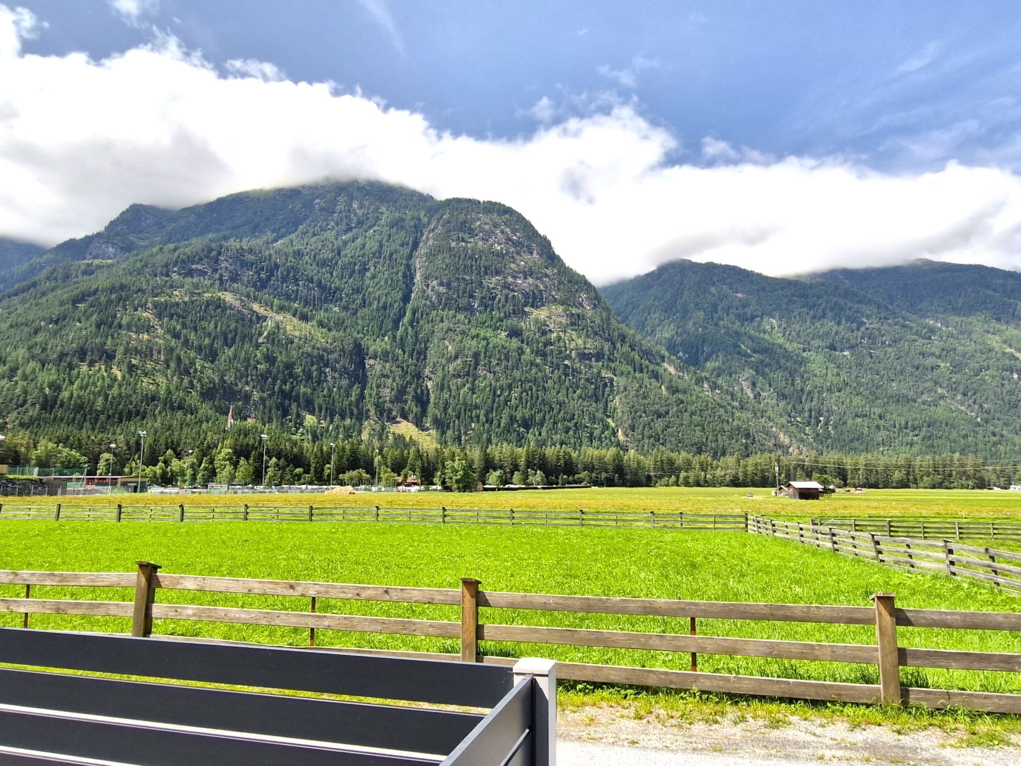 A view of a mountainous landscape with green fields and a wooden fence in the foreground.