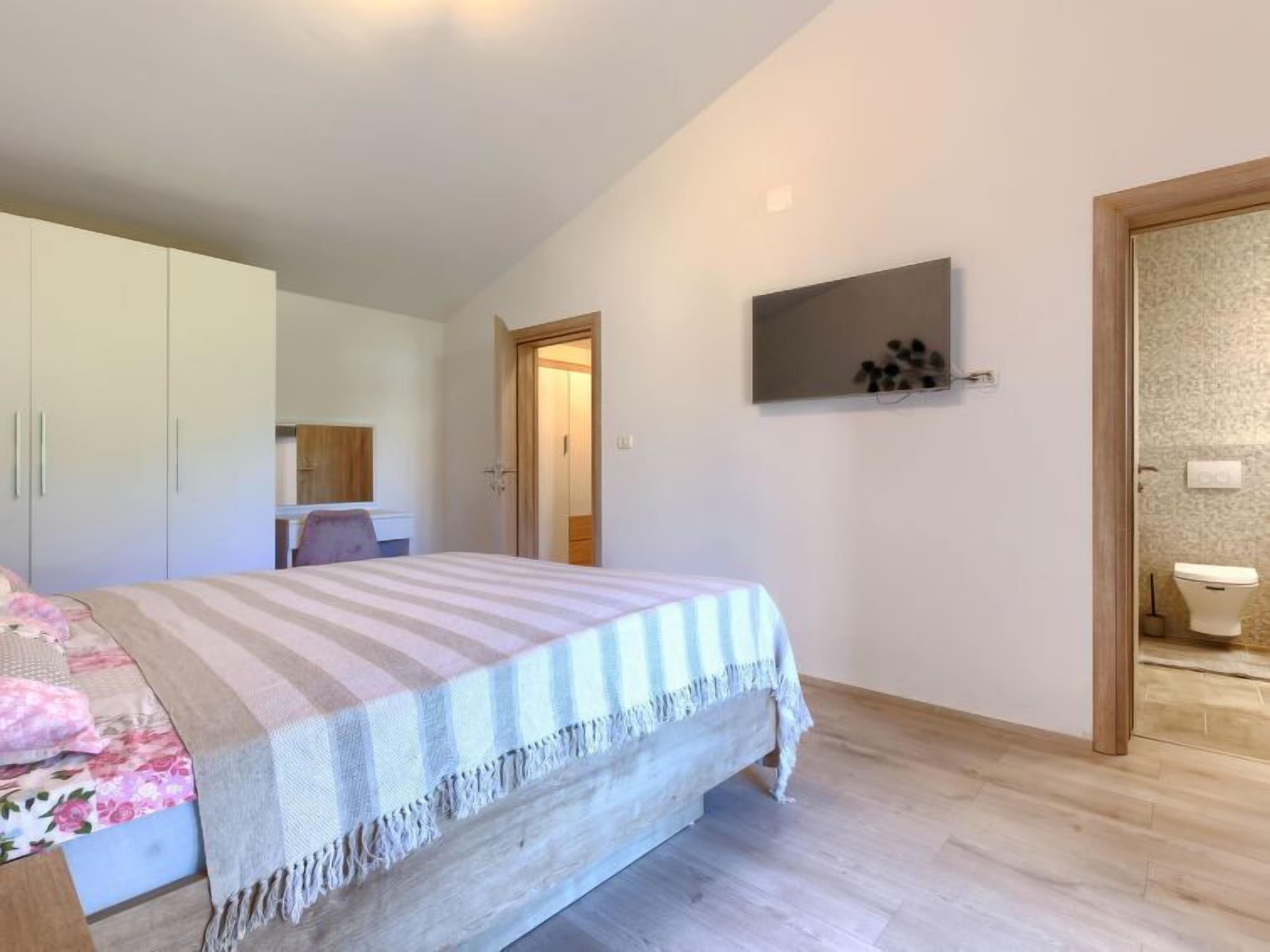 Ein Schlafzimmer mit Bett, Schrank, Spiegel, einer Tür zu einem Badezimmer und einem an der Wand hängenden Bild.