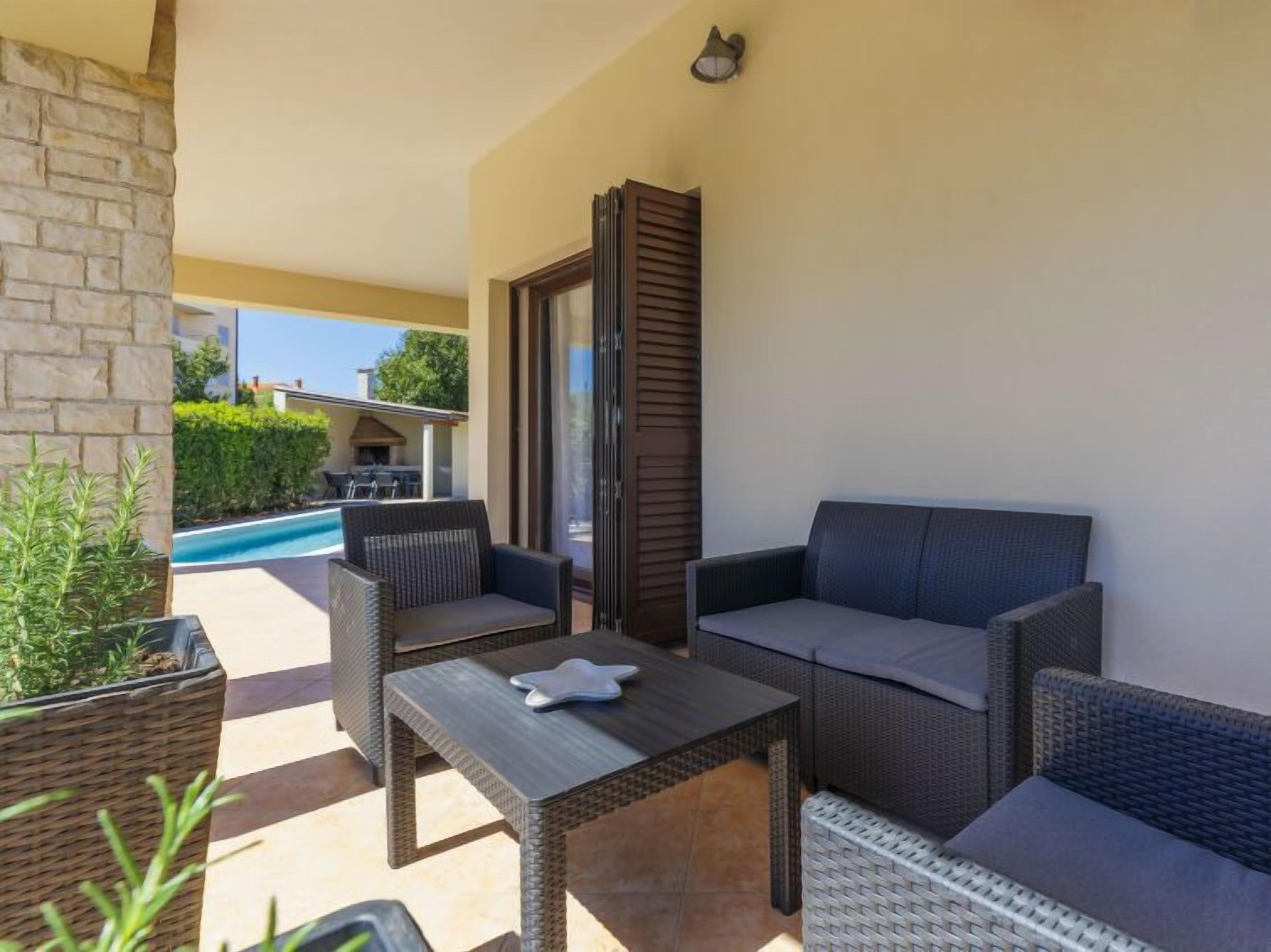 Una zona patio con mobili in vimini, una piscina e un muro in pietra.