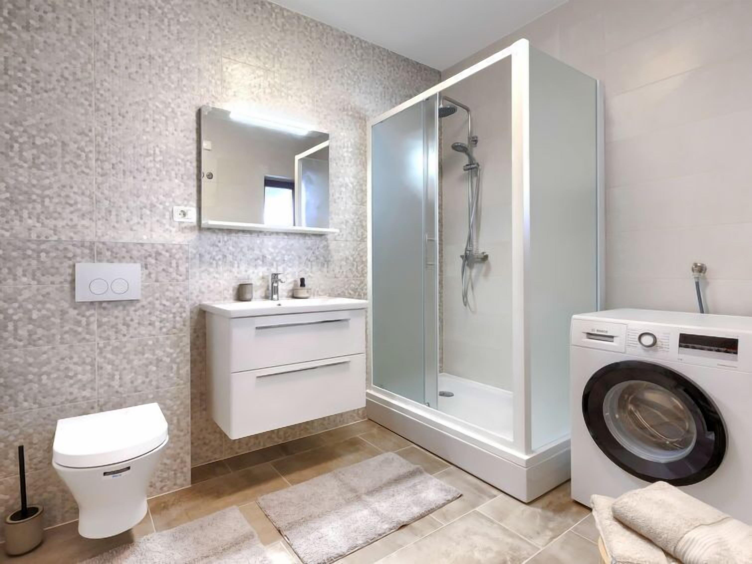 Une salle de bain moderne équipée d’une douche, de toilettes, d’un lavabo et d’un lave-linge.