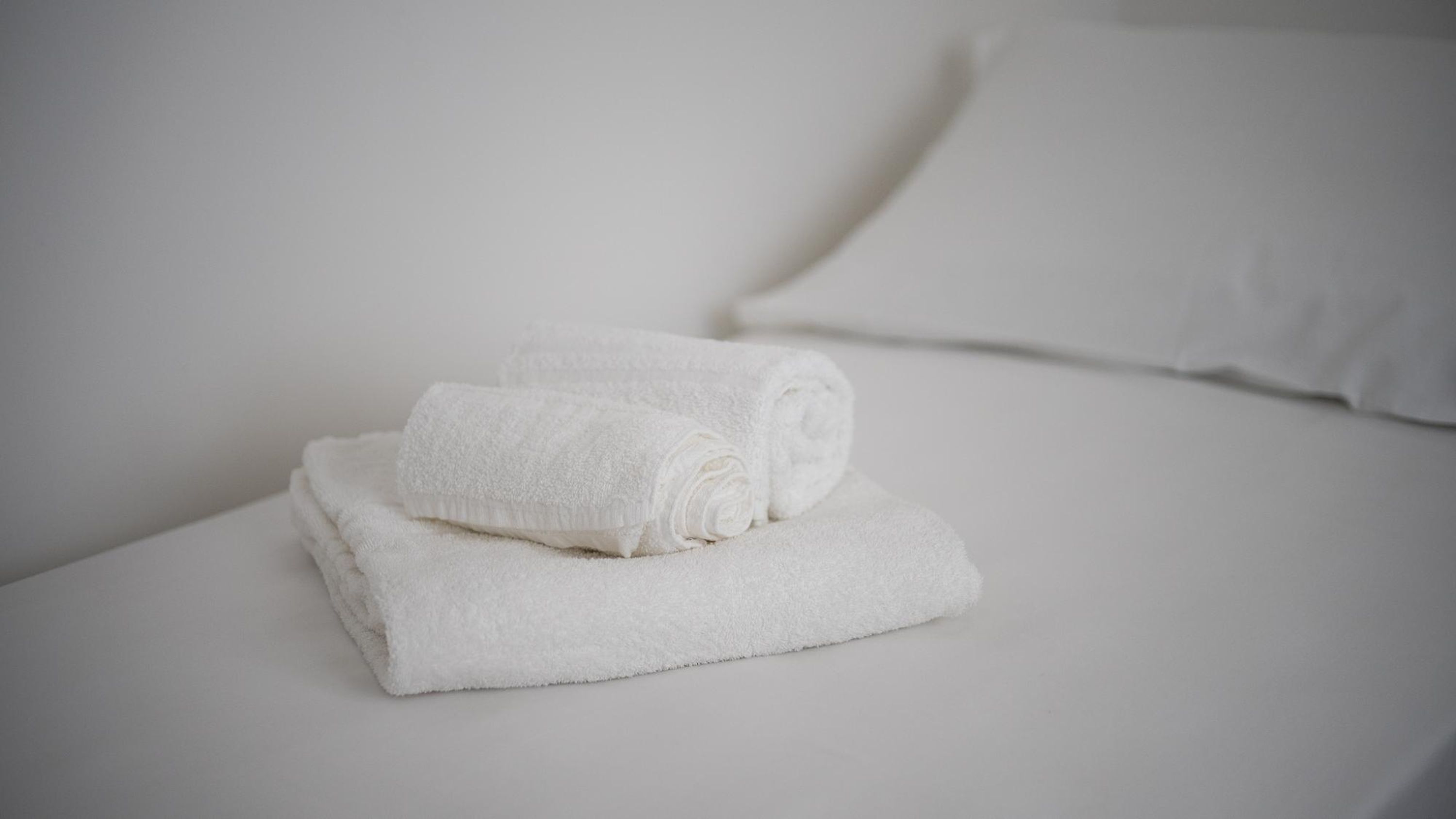 A neatly folded white towel on a bed with a white pillow.
