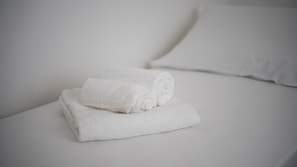 En prydligt vikt vit handduk ligger på en säng tillsammans med en vit kudde.