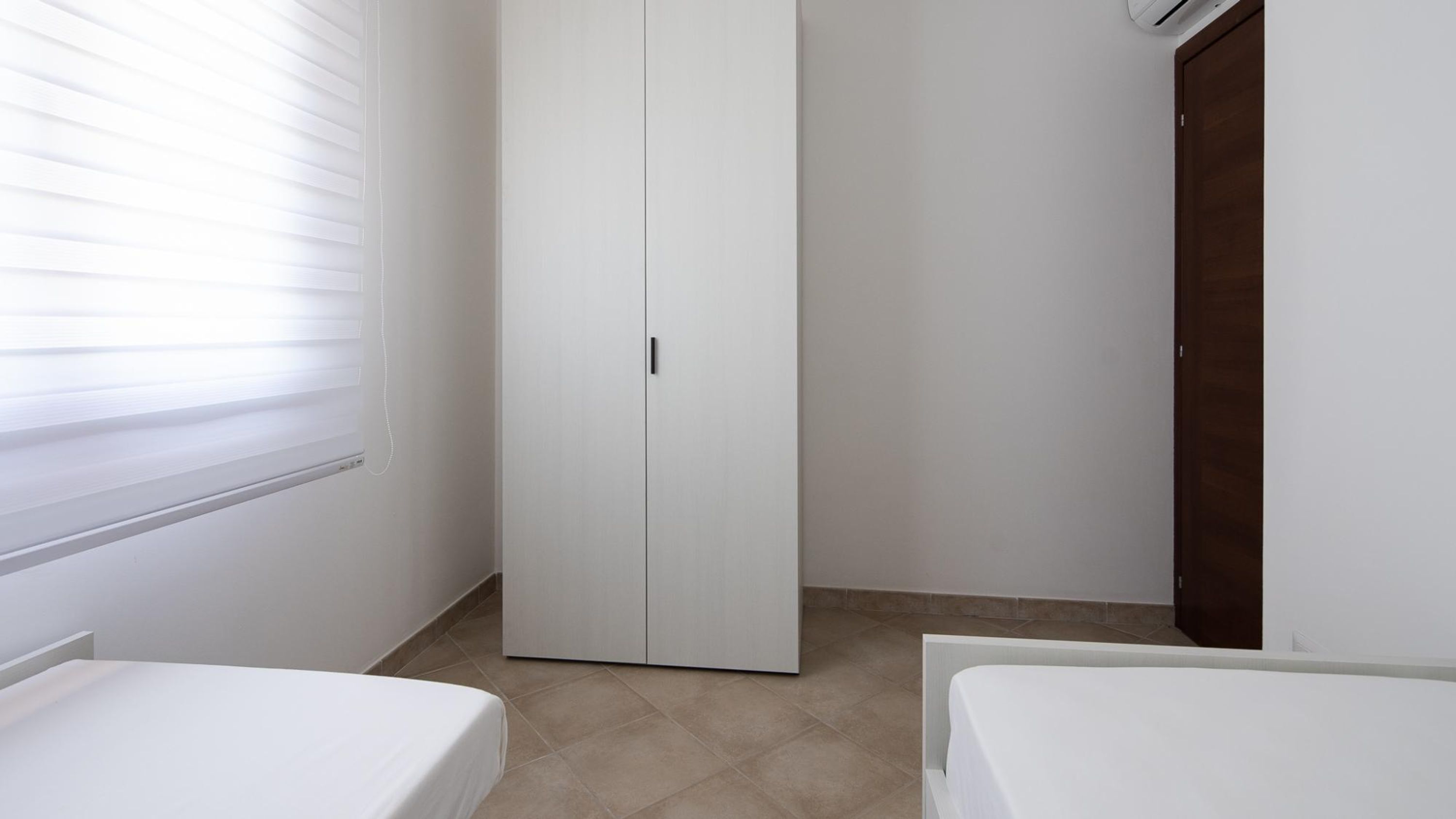 A bedroom with two single beds, a white wardrobe, and a wooden door.
