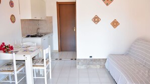 A compact living space with a kitchenette, a dining area with a table and chairs, and a sofa. - Welcomely - Villa Oleandro (Muravera)
