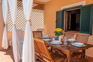 A wooden dining table set for four with white plates, glasses, and a vase of yellow flowers.