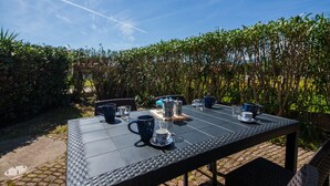 Mesa de comedor exterior con tazas azules, una cafetera y una bandeja.
