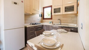 Una cocina moderna con refrigerador, estufa, lavaplatos y armarios. Hay una ventana sobre el lavaplatos, y una mesa con platos y vasos listos para comer.