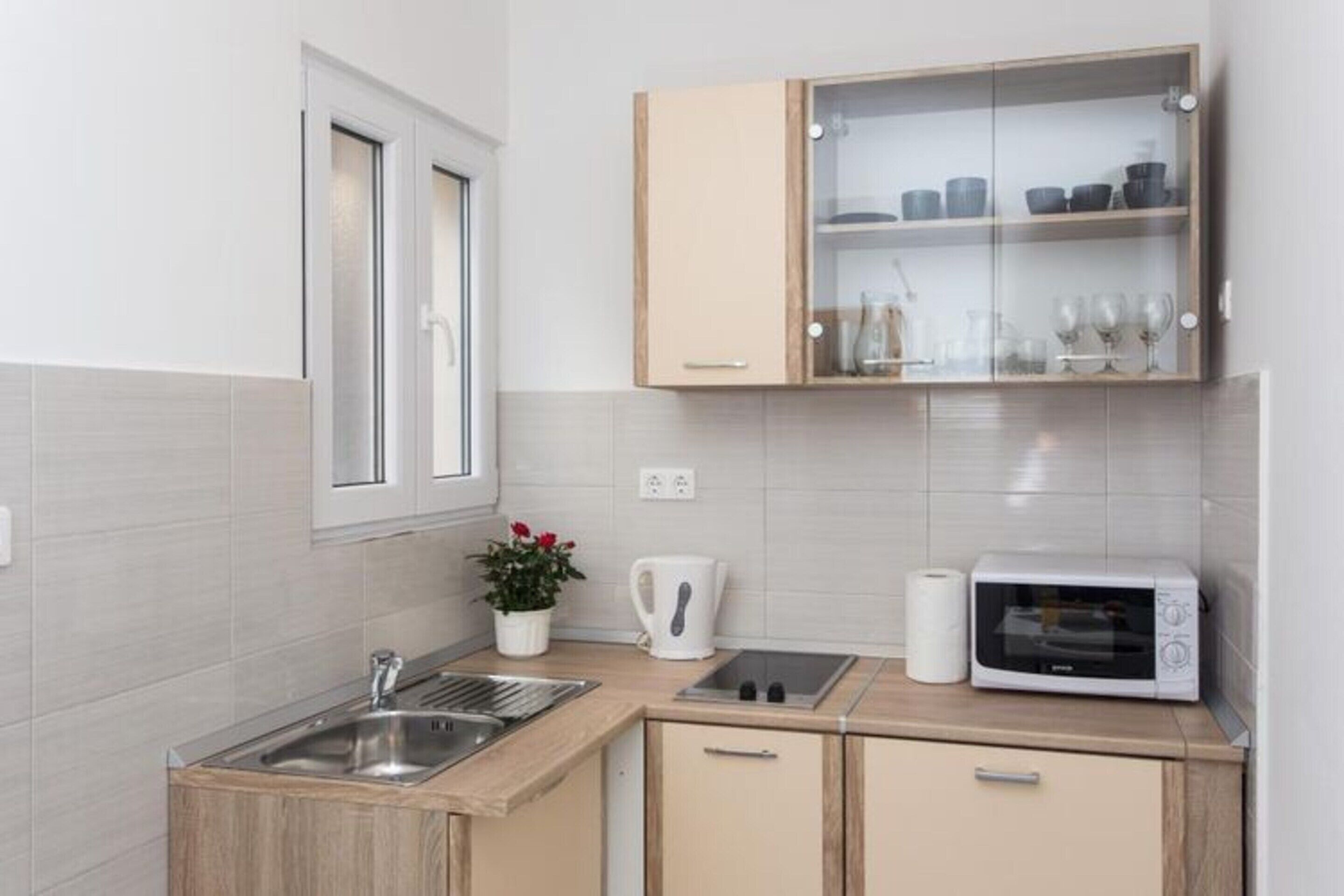Una cocina compacta con lavamanos, microondas y un armario con puertas de vidrio.